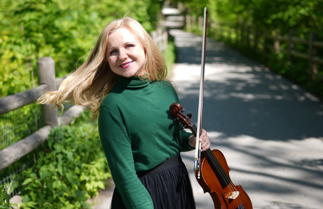 Olena Ponpon holding her violin and bow on a tree-lined path